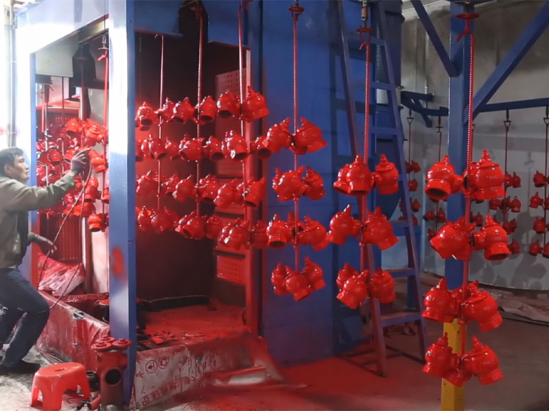 Red fire-hydrant bodies hanging inside an enclosed coating area