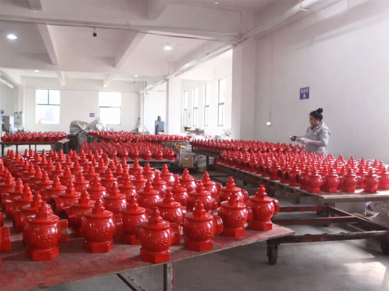 Rows of painted red hydrant bodies arranged on workshop tables beside a worker